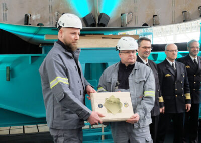 Werftmitarbeiter präsentieren Gedenktafel: Andre Loth und Heiko Schulz zeigen die eingebrachte Gedenkplatte zur Kiellegung der neuen Flottendienstboote. Foto: HSC