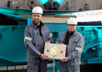 Werftmitarbeiter Andre Loth und Heiko Schulz mit der Gedenkmünze. Foto: HSC