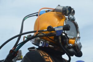 Taucher Dirk Schoenen bereitet sich auf seinen Einsatz vor. An seinem Helm sind Licht und Kamera montiert, sodass die Kollegen auf der Plattform „Baltic Lift“ seine Arbeit an Bildschirmen verfolgen können.