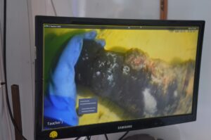 Fund: Taucher Dirk Schoenen hält eine am Ostseegrund gefundene Munition. Zu sehen ist das Video auf einem Bildschirm auf der Plattform „Baltic Lift“.