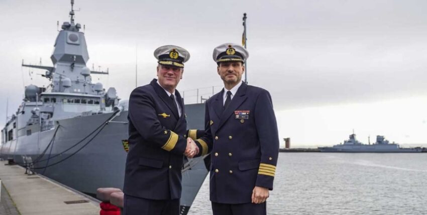 Der aktuelle Kommandeur Einsatzflottille 2, Flottillenadmiral Axel Schulz, und der aktuelle Chef des Stabes und designierte Kommandeur EF2, Kapitän zur See Sven Beck, posieren vor der Truppenfahne sowie vor der Fregatte "Sachsen". Foto: Bundeswehr / Rodewald